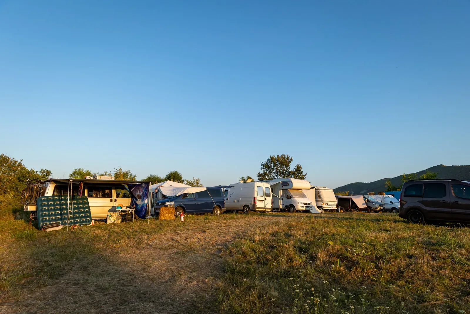 Kamperi u nizu na livadi sela, u pozadini šuma