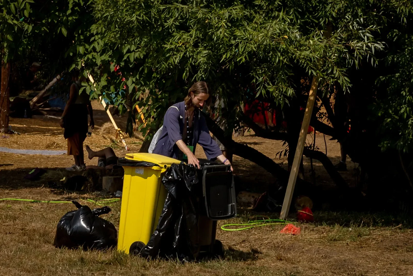 A volunteer sorting waste into bins in the shade