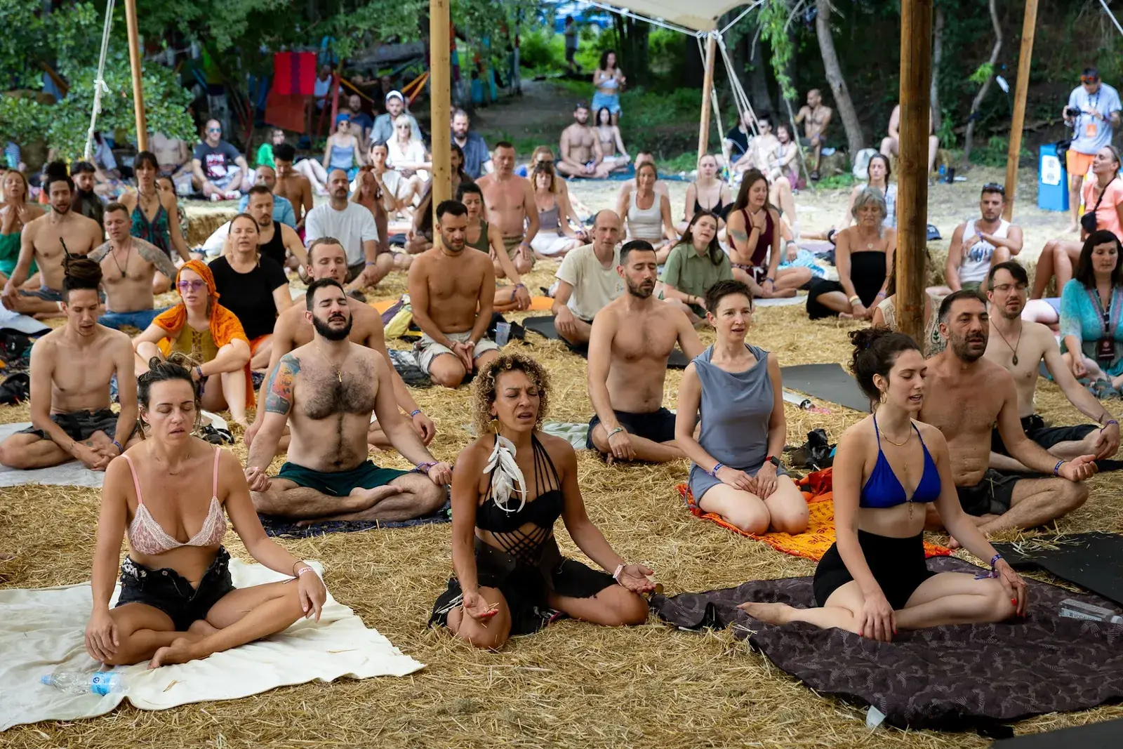 Velika grupa ljudi meditira sedeći na slami ispod šatora