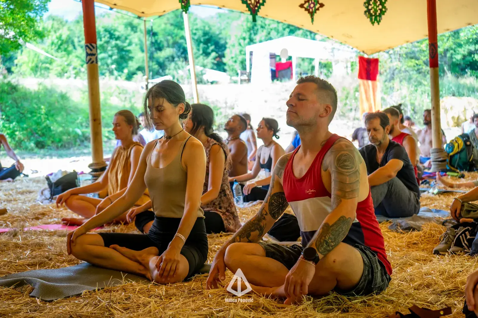 Grupa meditira na slami ispod šatora